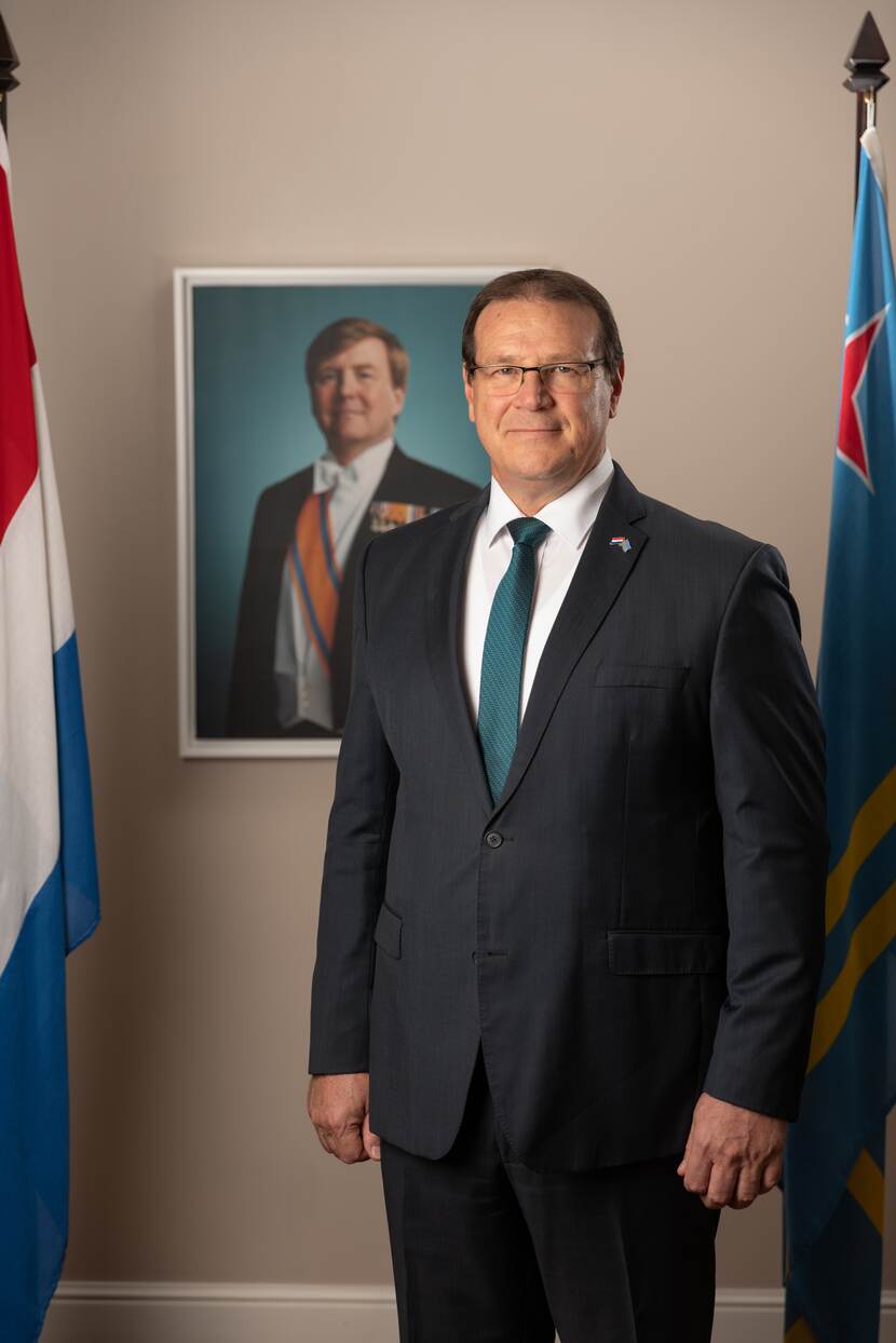 Portret di Gobernador Boekhoudt. Riba background tin un potret estatal di Rey Willem-Alexander. Na man robes di Gobernador tin e bandera Hulandes y na man drechi e bandera di Aruba.